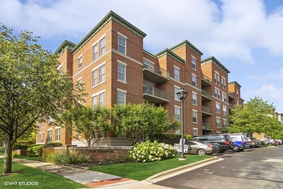 Front view of a multi-story brick residential building with balconies and adjacent parking area.