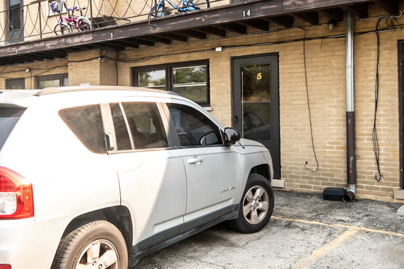 Outdoor parking area with a vehicle parked in front of a brick building entrance.