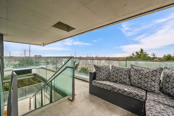 Balcony with glass railing and outdoor seating overlooking surrounding areas.