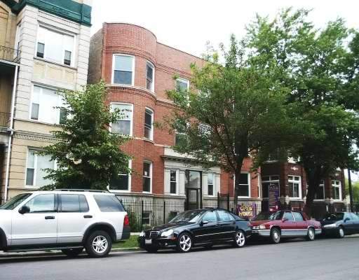 Front view of a three-story brick building with several windows and a tree-lined path.