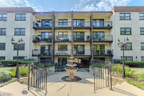 Front view of a four-story apartment building with balconies and a central fountain.
