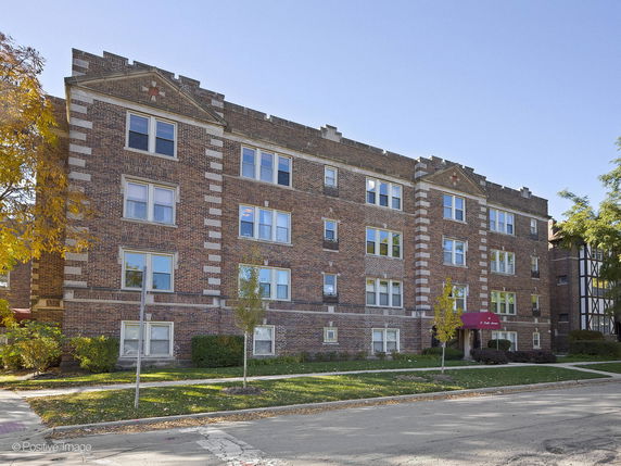 Front view of a multi-story brick apartment building with multiple windows and a central entrance canopy.
