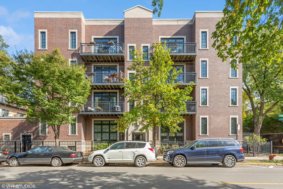 Front view of a multi-story brick apartment building with balconies and parked cars.