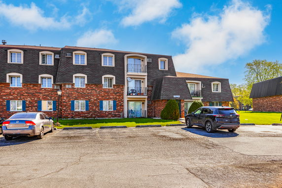 Front view of a multi-story residential building with brick facade and parking area.
