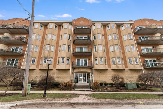 Front view of a multi-story condominium building with balconies and a central entrance.