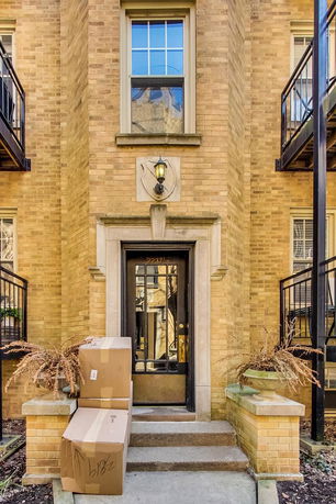 Front view of a brick building entrance with a black door and balcony railings.