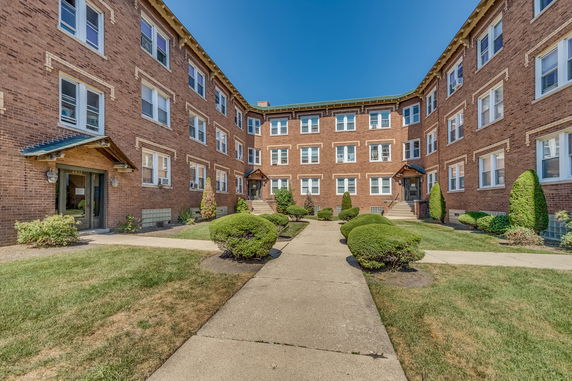 Front view of a three-story brick apartment building with landscaped entrance.