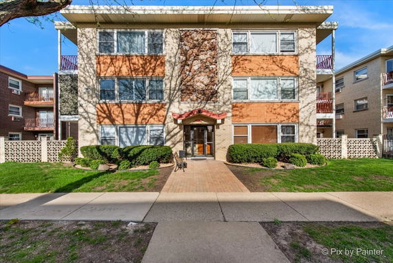 Front view of a multi-story apartment building with a central entrance and large windows.