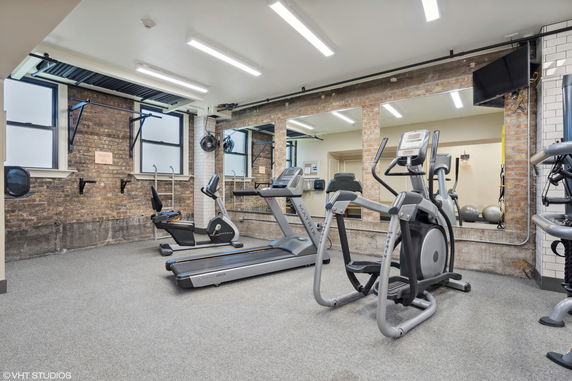 Indoor gym area with brick walls, mirrors, treadmills, and exercise equipment.