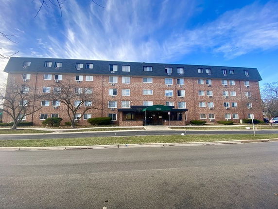 Front view of a four-story brick apartment building with a covered entrance.