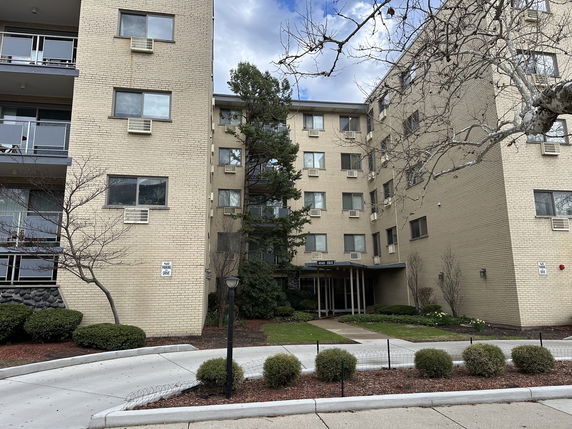 Front view of a multi-story apartment building with a beige brick exterior and entrance.