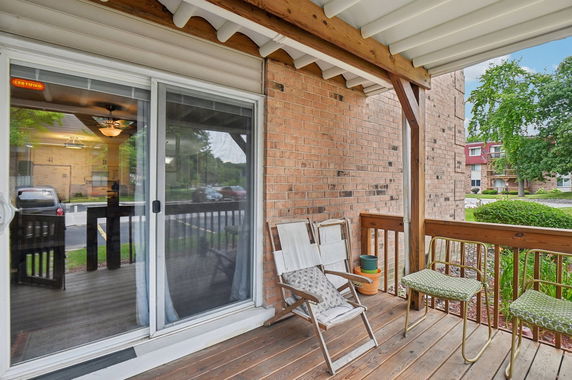 View from a porch with chairs, showing a parking area and nearby buildings.