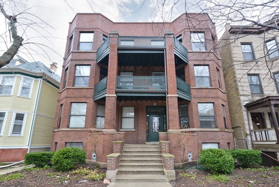 Front view of a three-story brick apartment building with balconies.