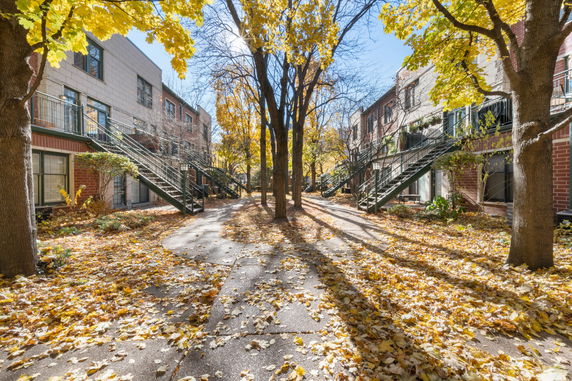 Front view of a multi-story residential building with external staircases and trees with autumn leaves.