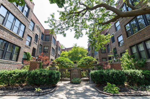 Front view of a brick apartment building with gated entrance and surrounding greenery.