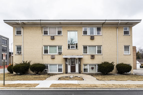 Front view of a three-story apartment building with beige brick exterior.
