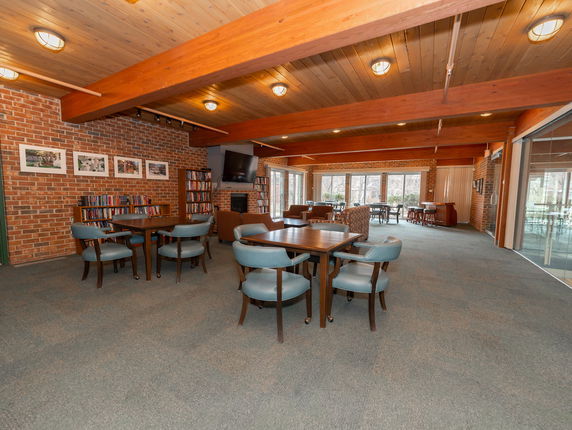 Room with brick walls, wooden beams, tables, chairs, and bookshelves.