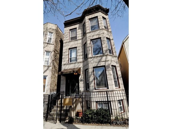 Front view of a three-story residential building with bay windows and a staircase entrance.