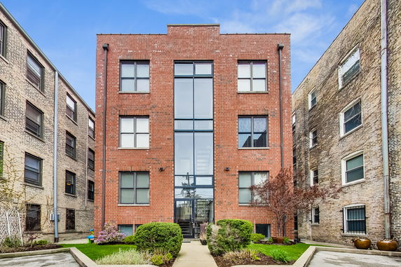 Front view of a three-story brick residential building with multiple windows and a central glass entryway.