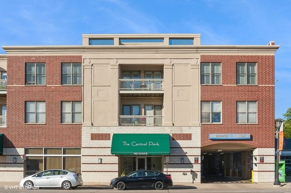 Front view of a multi-story building with a brick facade and multiple windows, featuring a central balcony and an entrance with a green awning.