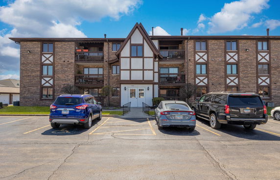 Front view of a multi-story apartment building with a brick facade and parking area in front.