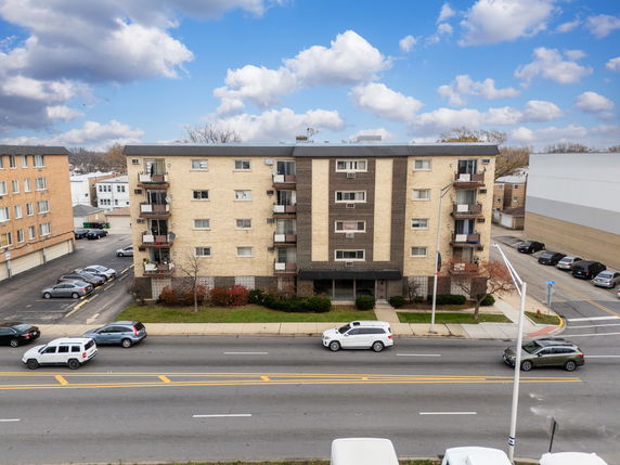 Front view of a multi-story apartment building with balconies and parking area.