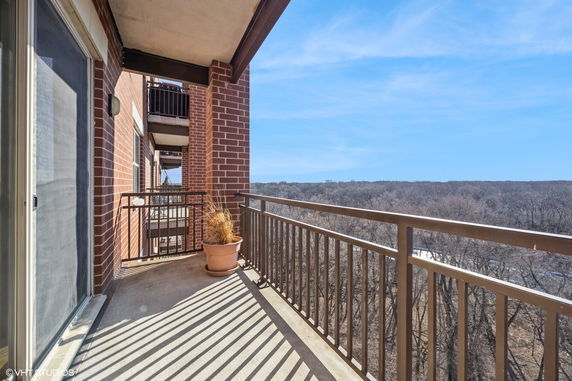 View from a balcony with railing and potted plant, overlooking a wooded area.