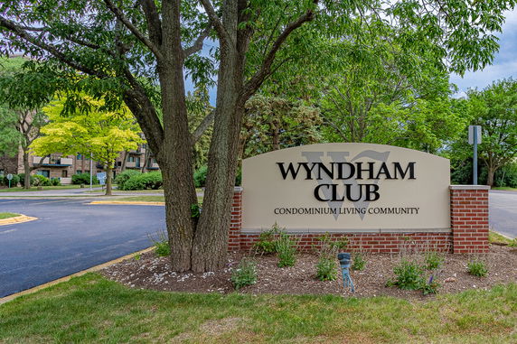 Front view of a condominium community sign with trees and a road in the background.
