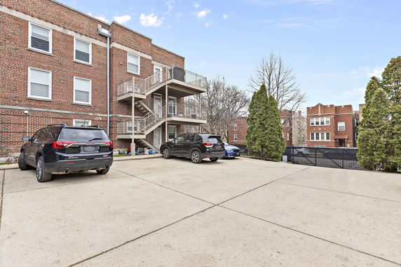 Outdoor parking area with multiple vehicles and a brick building with exterior staircases.
