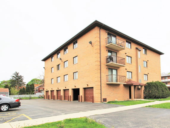 Front view of a four-story brick apartment building with balconies and garage entrances.