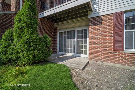 Rear view of a brick building with sliding glass doors leading to a small concrete patio.