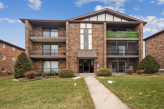 Front view of a three-story brick apartment building with balconies.