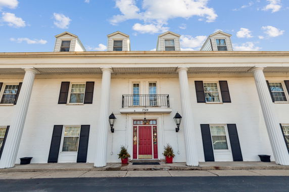 Front view of a building with white columns and a red door.