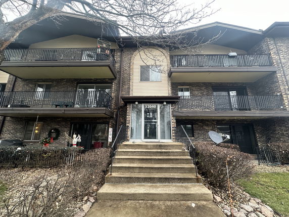Front view of a multi-story building with balconies and a central entrance staircase.