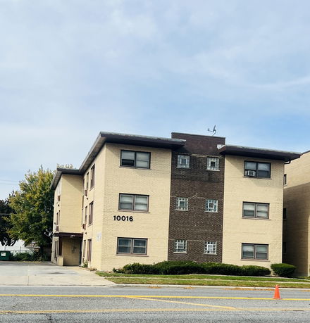 Front view of a multi-story apartment building with beige and brown brick exterior.