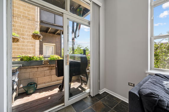 View through glass door to a small outdoor space with plants and a barbecue grill.