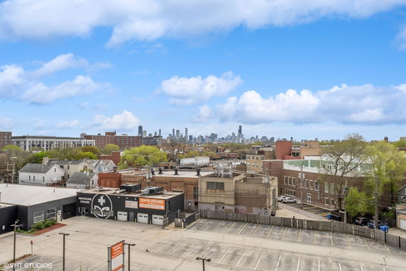 Wide-angle view of urban buildings with a distant city skyline under a blue, cloudy sky.