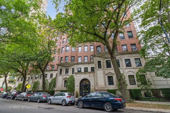 Front view of a multi-story brick building with decorative stone façade and large trees in front.