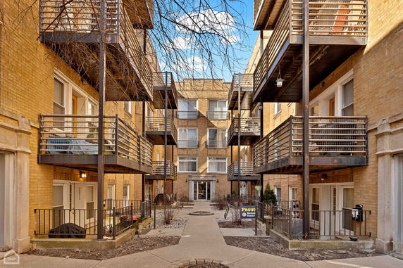 View of the exterior of an apartment building with balconies and entrance pathway.