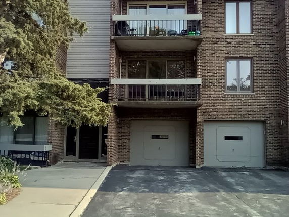 Front view of a multi-story brick building with balconies and two garage doors.