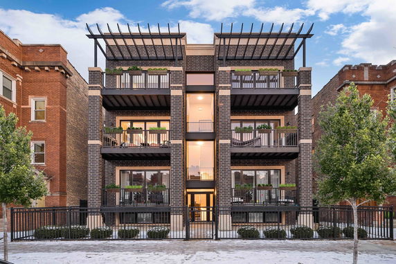 Front view of a modern multi-story building with balconies and a fenced entrance.