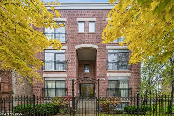 Front view of a multi-story brick building with iron balconies and a gated entrance.