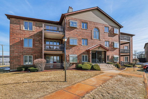 Front view of a three-story brick apartment building with balconies.