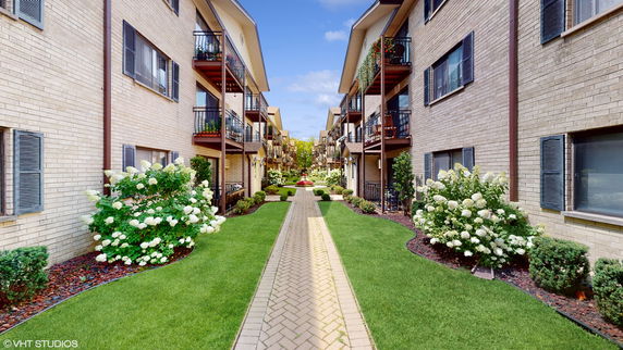 Front view of multi-story apartment buildings with balconies and landscaped pathways.