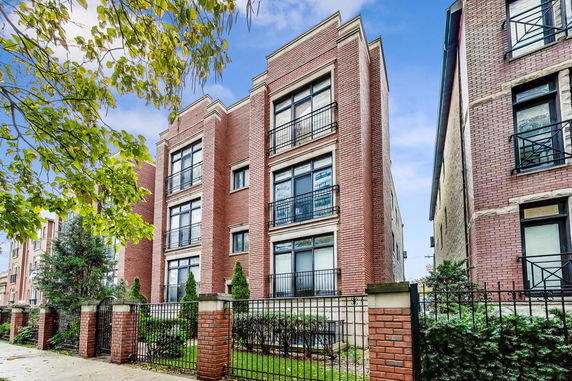Front view of a multi-story brick building with balconies and a fenced yard.