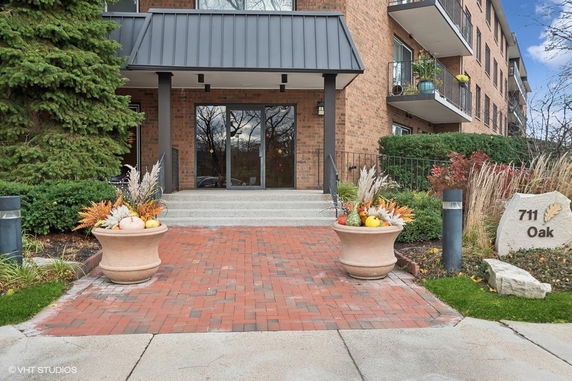 Front view of a brick residential building with balconies and entrance pathway.