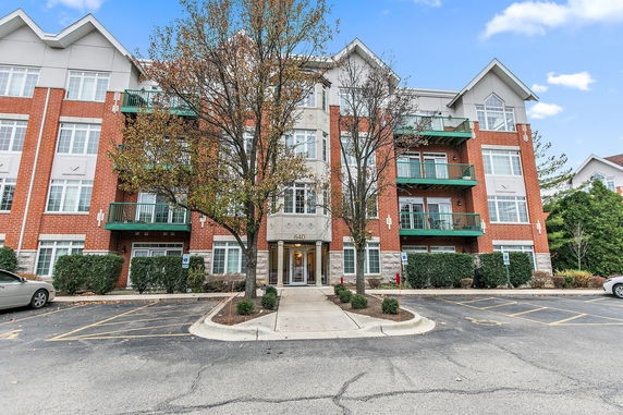 Front view of a multi-story apartment building with red brick exterior and green balconies.