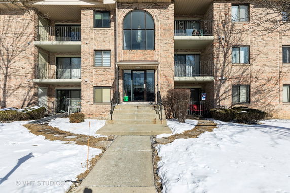 Front view of a multi-story brick apartment building with balconies and a central entrance.