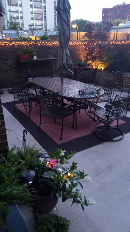 Rooftop patio with dining table and chairs, surrounded by decorative lighting and plants.