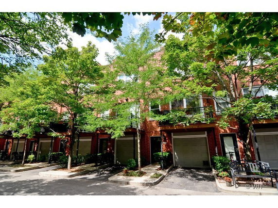 Front view of a row of townhouses with garages and trees in front.